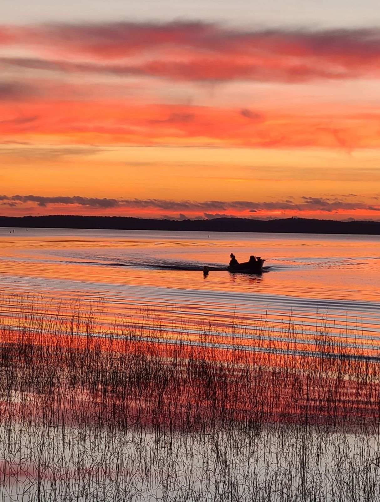 Deux silhouettes avançant ensemble sur l'eau, sous un ciel flamboyant
