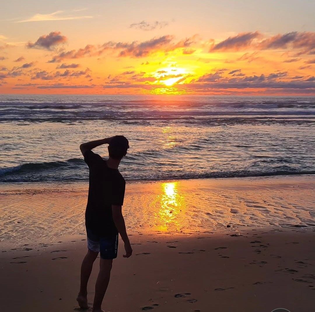 Silhouette d'une personne sur une plage, main en visière, regardant le soleil se coucher sur l'océan